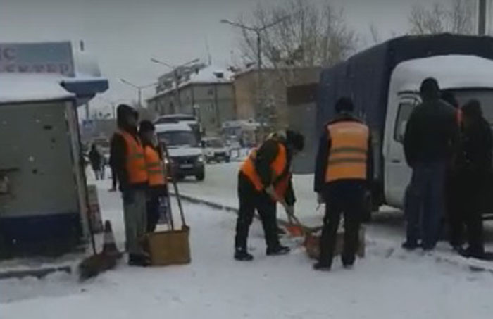 Люди в спецодежде сгребают лопатами снег… в картонные коробки.